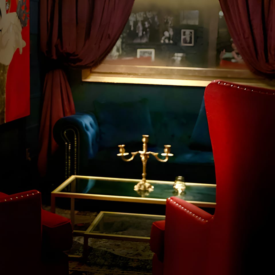 Dark, luxurious lounge area with red velvet chairs, a blue sofa, and a gold candelabra on a coffee table.