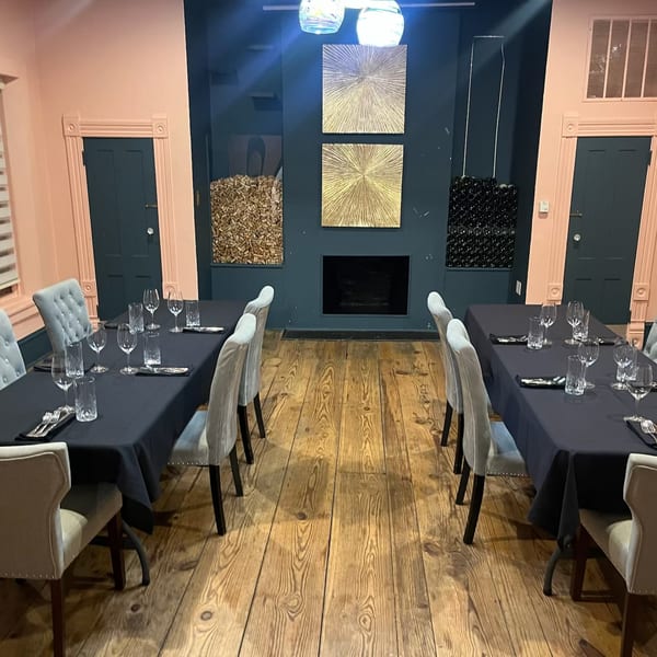 Two long dining tables set with black tablecloths and light chairs in a private dining room.