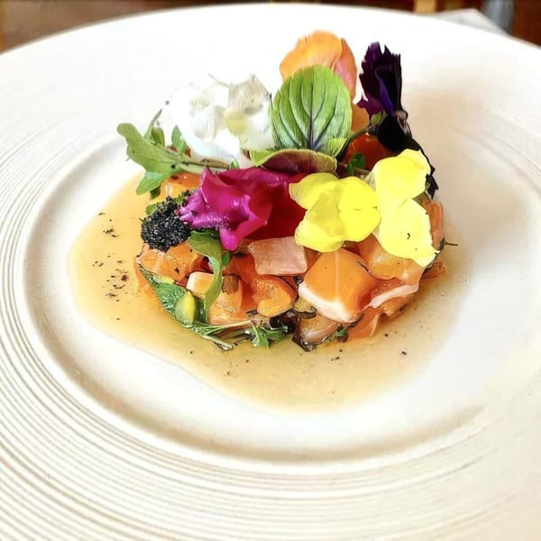 A colorful appetizer with edible flowers, greens, and diced salmon in a light sauce on a white plate.