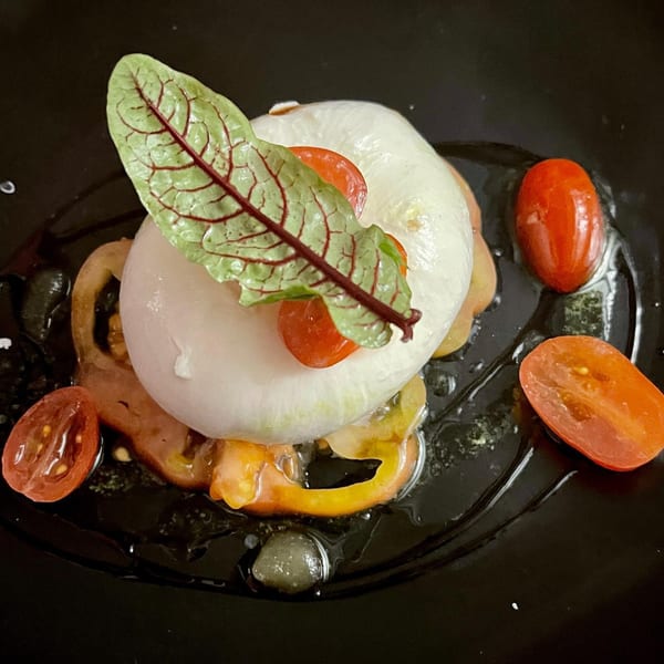 A caprese salad with a large ball of mozzarella, cherry tomatoes, and a green leaf on a dark plate.