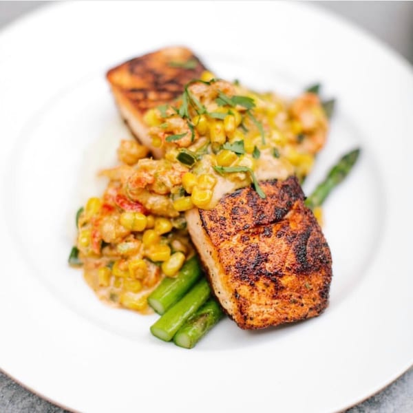 Blackened fish with corn and shrimp relish, served with asparagus on a white plate.
