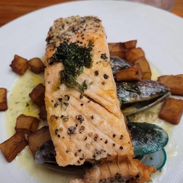 Pan-seared salmon with mussels, crispy potatoes, and a creamy sauce on a white plate.