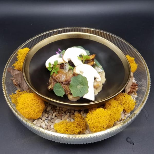 Gourmet mushroom dish with large white mushroom slices, greens, and small purple flowers in a black bowl.