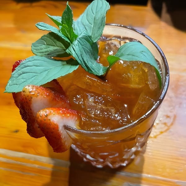 A refreshing cocktail with ice, garnished with fresh mint and sliced strawberries on a wooden table.