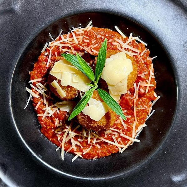 Fried arancini balls with tomato sauce, shredded and shaved parmesan, and fresh mint in a black bowl.