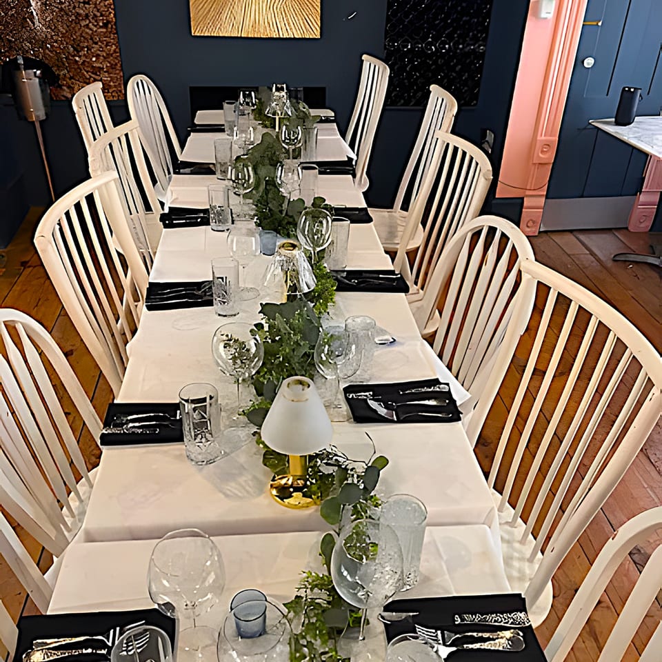 A long dining table set with white tablecloths, black napkins, and green garland centerpieces.